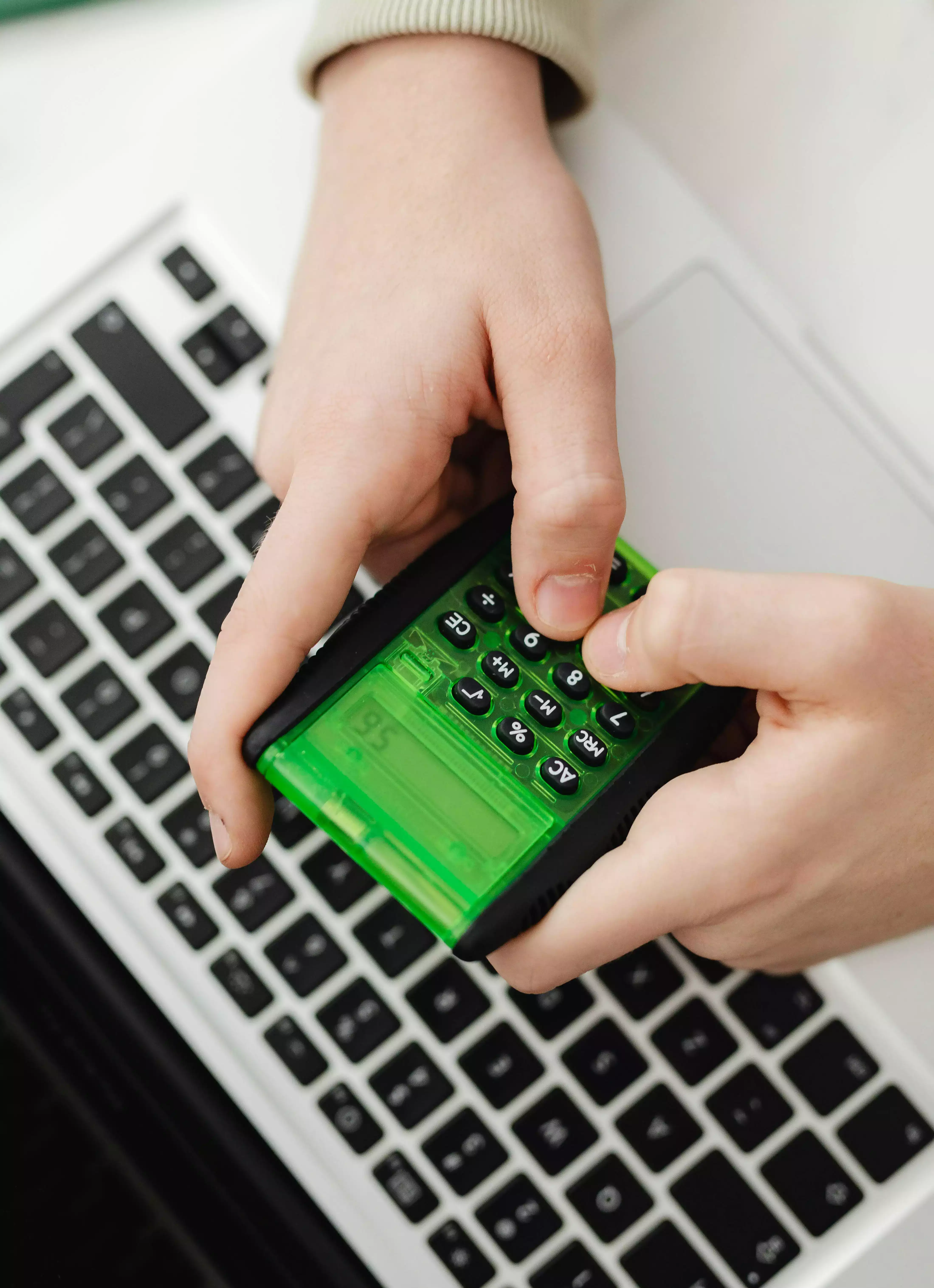 Pessoa digitando em uma calculadora verde em cima de um notebook